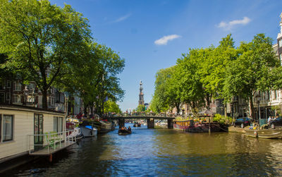 Boats moored on river by trees against sky in city