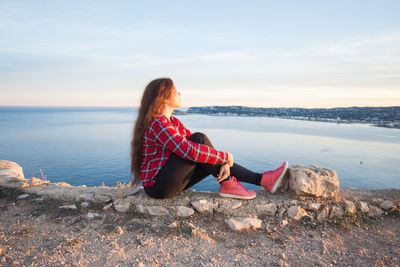 Woman sitting on rock by sea against sky