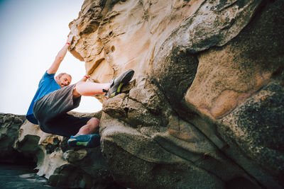 Man climbing on rock formation against sky