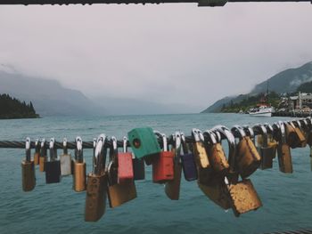 Close-up of padlocks hanging on sea against sky