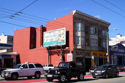 Cars on road by buildings against sky in city