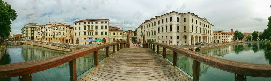 Panoramic view of river with bridge by buildings against cloudy sky