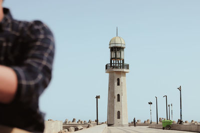 Midsection of man standing by lighthouse against clear sky