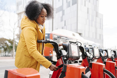 Young woman unlocking bicycle through mobile phone at station