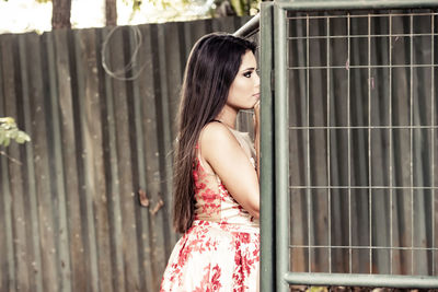 Side view of young woman looking through fence
