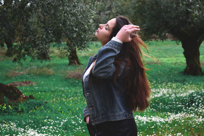 Side view of beautiful young woman with hand in hair standing at park