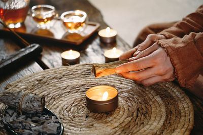 Woman hands burning palo santo, before ritual on the table with candles and green plants. smoke of