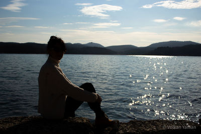 Man sitting by sea against sky