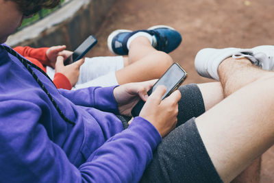 Low section of male friends using phones while sitting outdoors