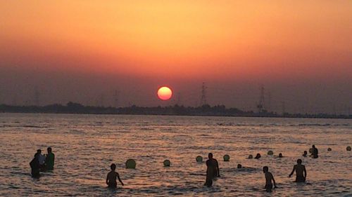 Silhouette people on beach against sky during sunset