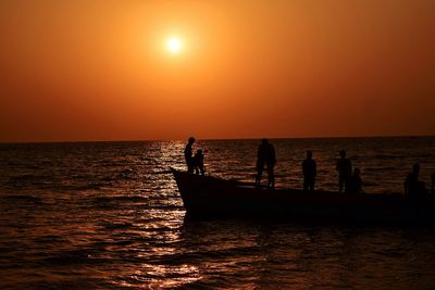 Silhouette people on sea against sky during sunset