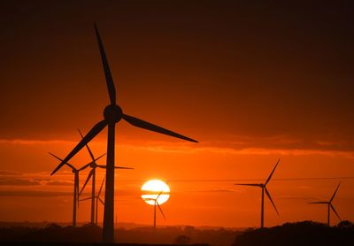 Silhouette wind turbines on field against orange sky