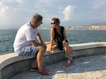 Friends sitting on sea shore against sky