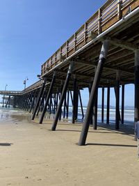 Low angle view of pier on beach against clear blue sky