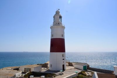 Lighthouse by sea against clear blue sky