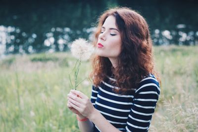 Beautiful woman blowing dandelion on field