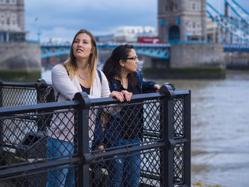 Smiling female friends standing by railing in city