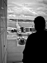 Rear view of man on airplane at airport runway against sky