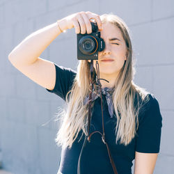 Portrait of young woman photographing against wall