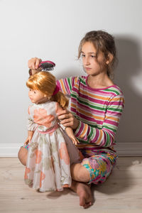 Cute girl combing doll hair at home