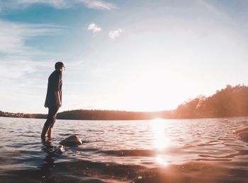 Young man standing in lake against sky during sunset