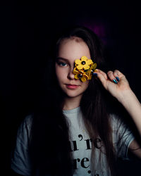 Portrait of young woman holding sunglasses against black background