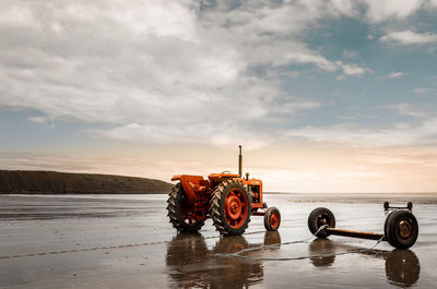 Red tractor on the beach at sunset