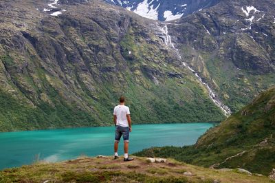 Rear view of man standing by lake against rocky mountains