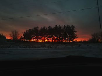 Silhouette trees on landscape against sky during sunset