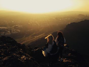 Rear view of woman sitting on rock against sky during sunset