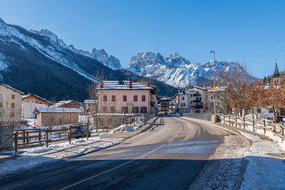 Snow covered road by buildings against sky