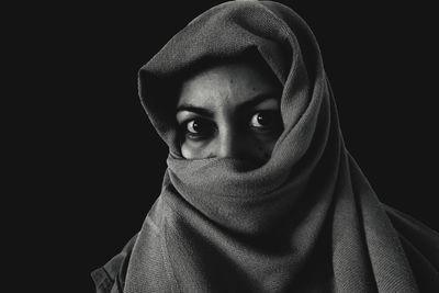 Portrait of young woman covering face against black background