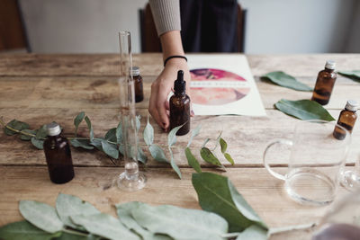 Cropped hand of female owner holding perfume bottle on table at workshop