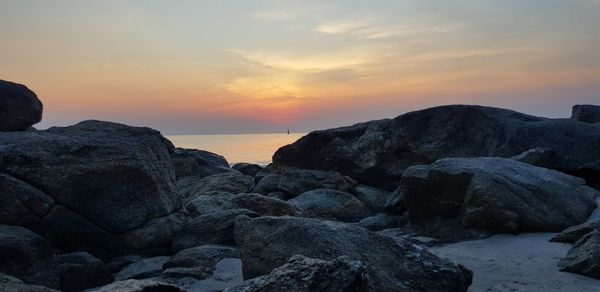 Rocks on beach against sky during sunset