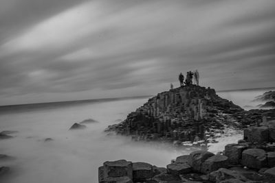 People standing on rock by sea against sky