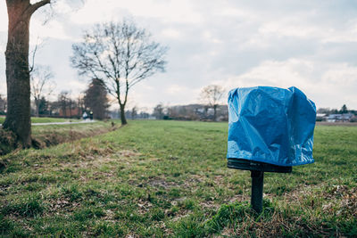 Garbage can with blue plastic bag in front in front of trees