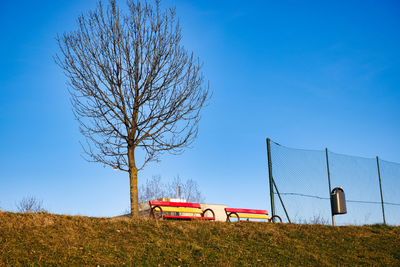 Bare tree on field against clear blue sky