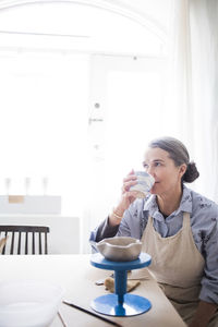 Senior female potter smelling vase while sitting at workbench in store