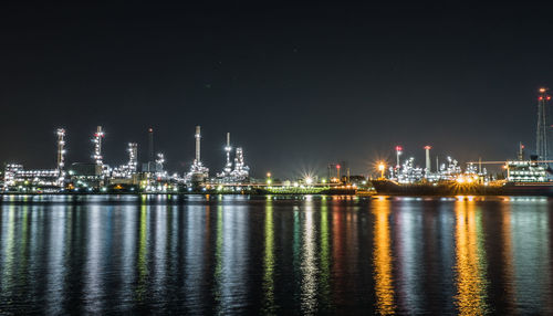 Illuminated city by sea against sky at night