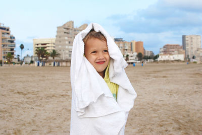 Portrait of little boy wrapped in towel standing at beach