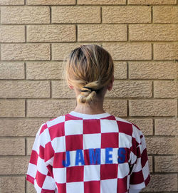 Rear view of woman standing against brick wall