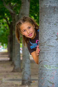 Portrait of smiling girl playing on tree trunk