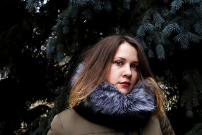 Portrait of young woman standing against trees