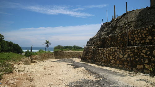 Stone wall by road against sky