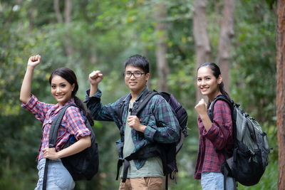 Portrait of friends clenching fists against trees