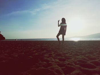 Rear view of woman standing on beach against sky