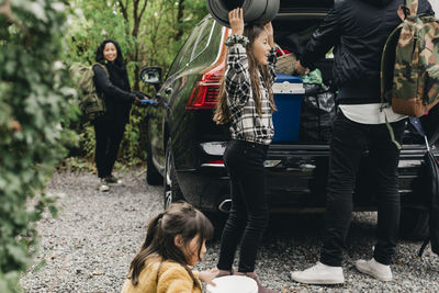 Daughter with parents loading luggage in electric car trunk