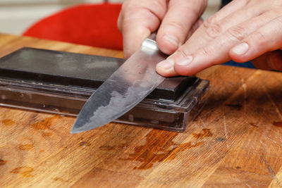 Cropped hand of person sharpening knife on table