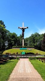 Statue on footpath in park against blue sky