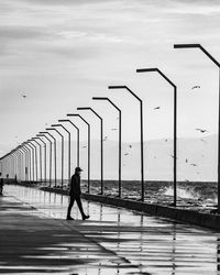  black and white rear view of man walking on bridge